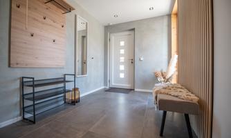 A modern hallway with gray walls and a light floor. A wooden coat rack and a cozy stool give the room an inviting character.