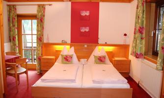 A cozy bedroom with a double bed and colorful curtains. The room features wooden details and a small table with chairs.