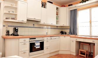 A modern kitchen with white cabinets and wooden countertops. There is a window seat with plenty of natural light and a coffee machine on the countertop.