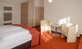A cozy hotel room with a large bed and a small table. Two chairs are placed next to the table, and the room has a warm tone.