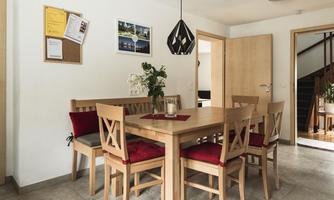 A cozy dining area with a wooden table and chairs in neutral colors. A plant and wall decoration give the room an inviting atmosphere.
