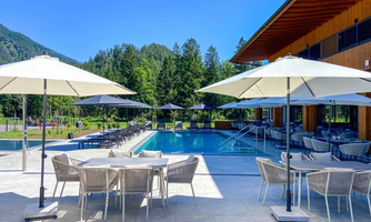 A beautiful swimming pool with lounge chairs and sun umbrellas. Surrounded by green mountains and a clear blue sky.