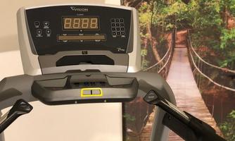 A modern treadmill with a digital display. In the background, there is a green landscape with a wooden walkway.