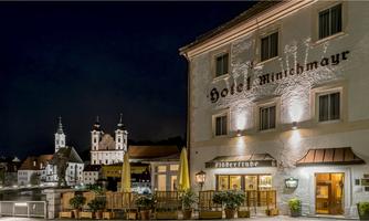 A charming hotel with a brightly lit facade at night. In the background, historic buildings are visible, contributing to the special atmosphere.