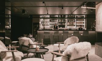 An elegant bar with stylish furniture and a well-stocked drink wall. The room has a cozy atmosphere with comfortable seating and subdued lighting.
