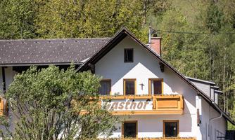 A cozy guesthouse with wooden balconies and a beautiful view of the surrounding nature. The facade is bright and friendly, surrounded by trees and green land.
