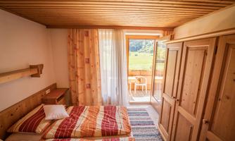 A cozy room with two beds, wooden paneling, and a balcony. Bright light streams through the windows, offering a view into the greenery.
