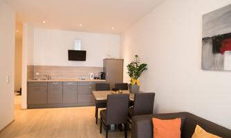 A modern kitchen with a dining area and a cozy living room. The decor is simple and elegant, with light colors and some plants.