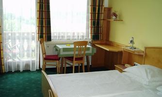 A cozy hotel room with a double bed and a table. The walls are yellow, and there are large windows with curtains.
