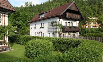 A cozy house surrounded by well-maintained greenery. In the background, trees and hills are visible.