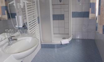 A modern bathroom with a shower and a sink. The floor is blue tiled and there is a red trash can.