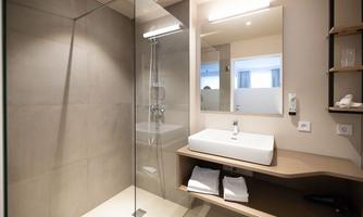 A modern bathroom with a glass shower and an elegant sink. The walls are in neutral colors and there are fresh towels on a shelf.