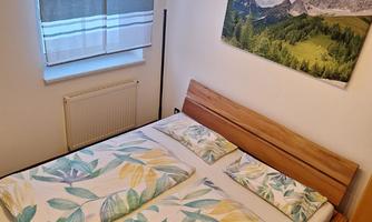 A cozy bedroom with a double bed and colorful bed sheets. A landscape painting hangs on the wall, and there are windows with elegant curtains.