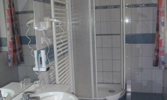 A modern bathroom with a shower and a sink. The walls are tiled and there is a large mirror.