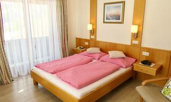 A cozy bedroom with a double bed and checked bed linens. The room has large windows, soft colors, and a pleasant atmosphere.