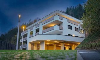 A modern building with several levels and large windows. The surroundings are quiet and green, with streetlights illuminating the area.