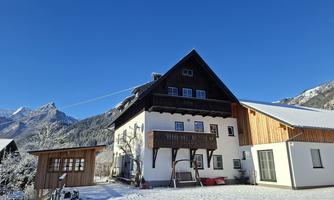 A charming house in the snow with a clear blue sky. The surrounding mountains add a picturesque backdrop.