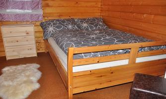 A cozy bedroom with a wooden bed and a gray duvet. Next to the bed is a wooden nightstand and a soft rug lies on the floor.