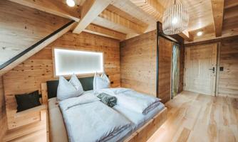 A cozy bedroom with a wooden ceiling and floor. The bed is decorated with white linens and pillows, and there is soft lighting.