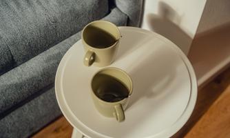 Two green cups are on a white table. In the background, a gray couch can be seen.