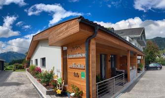 A charming holiday apartment with wooden paneling and green plants. The sky is clear and blue, surrounded by mountains.