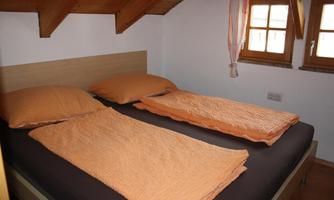 A cozy bedroom with a double bed and orange bedspreads. The windows let in plenty of daylight.