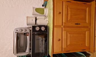 A small kitchenette with a wooden cabinet, on which a microwave oven, a coffee maker, and a kettle are placed. The colors are bright and cheerful.