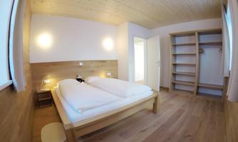 A simple bedroom with a double bed and wooden walls. The space is bright and has room for a wardrobe.