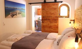A cozy bedroom with a large bed and wooden details. On the wall hangs a picture of a beautiful coastal landscape.