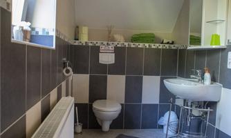 A modern bathroom with gray and white tiles. It contains a toilet, a sink, and some green towels.