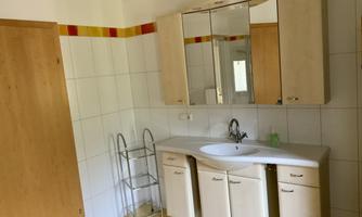 A modern bathroom with a sink, a mirror, and simple furniture. The walls are brightly tiled, and there is a towel rack.