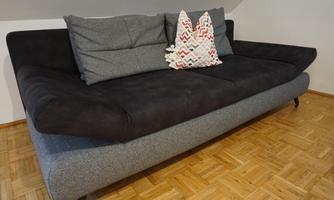 A modern gray sofa with two decorative cushions. The floor is made of wood with a light parquet pattern.