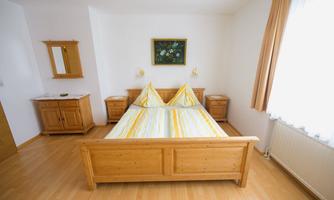A bright bedroom with a large wooden bed and yellow striped bedspreads. Next to the bed are two nightstands and a mirror on the wall.