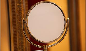 A decorative hand mirror with a round, empty mirror glass. The background is in warm colors.