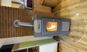 A modern wood stove stands in front of a brick wall. The fire burns and creates a cozy atmosphere in the room.