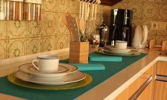 A well-designed kitchen with an inviting table setting. On the countertop, there are plates, cups, and kitchen utensils, surrounded by a decorative wall tile.