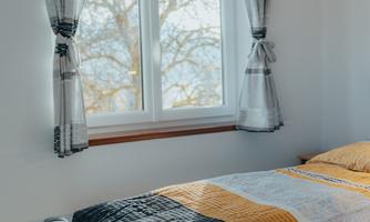 A bright bedroom with a window and modern curtains. On the bed are blankets and pillows in soft colors.