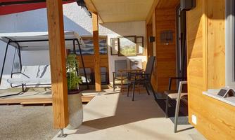 An inviting outdoor area with wooden cladding and a table with chairs. In the background, there is a swing and a pleasant, sunny atmosphere.