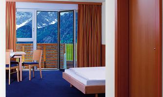 A bright room with wooden furniture and a view of the mountains. Large windows let in plenty of daylight.