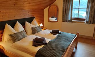 A cozy bedroom with two beds, equipped with pillows and towels. The wooden paneling and the large window create a warm atmosphere.