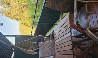 A balcony with a table and two chairs. In the background, trees and a green landscape can be seen.