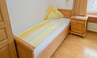 A cozy room with a wooden single bed. The bedding is striped in yellow and white.
