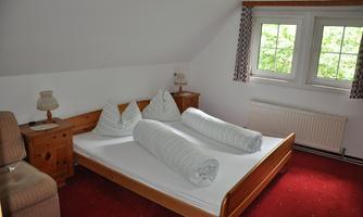 A cozy bedroom with a large bed and two big pillows. The room has a red carpet and plenty of daylight through the windows.