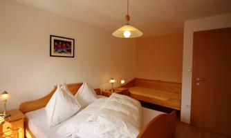 A cozy bedroom with a double bed and additional sleeping options. The walls are painted in soft colors and there is pleasant lighting.