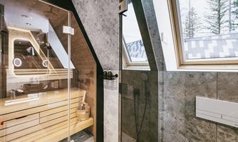 A modern shower with glass sliding doors and a wooden shelf. Large windows provide a view of trees and bring natural light into the room.