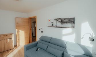 A bright room with a blue sofa and a wooden chest of drawers. On the wall hangs a picture that shows a boy with a balloon.