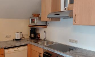 A modern kitchen with wooden cabinets and a bright countertop. The equipment includes a stove, a dishwasher, and a coffee machine.