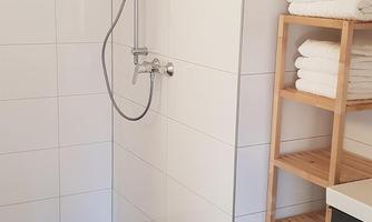 A modern bathroom with a shower cubicle and tiled wall. On the right, there is a shelf with fresh towels.