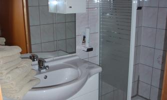 A small bathroom with a shower and a sink. Towels are neatly stacked on a shelf.
