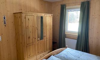 A cozy bedroom with wood paneling. There is a bed, a wardrobe, and a window with curtains.